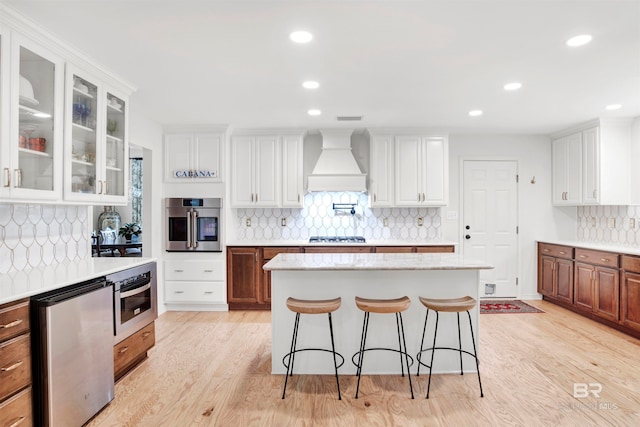 kitchen featuring light hardwood / wood-style floors, white cabinets, custom exhaust hood, and backsplash