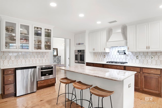 kitchen with white cabinetry, custom range hood, and stainless steel appliances