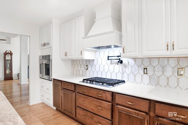 kitchen with appliances with stainless steel finishes, light hardwood / wood-style flooring, premium range hood, tasteful backsplash, and white cabinetry