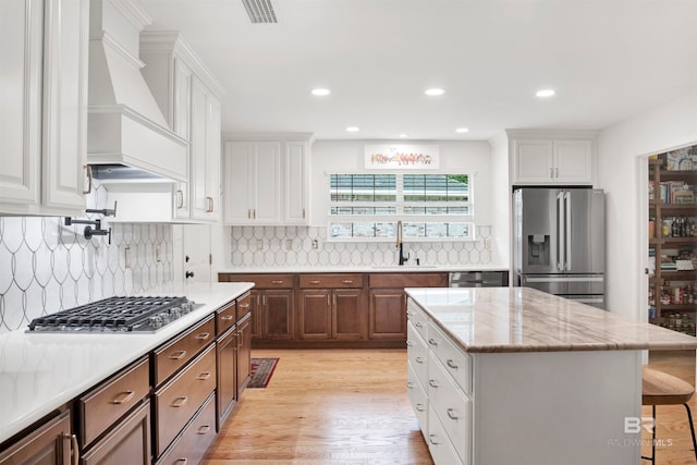 kitchen featuring a kitchen island, backsplash, stainless steel appliances, premium range hood, and white cabinetry