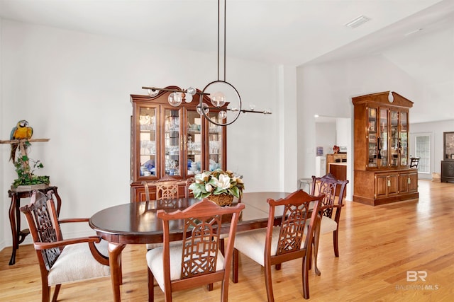 dining room with an inviting chandelier, vaulted ceiling, and light hardwood / wood-style flooring