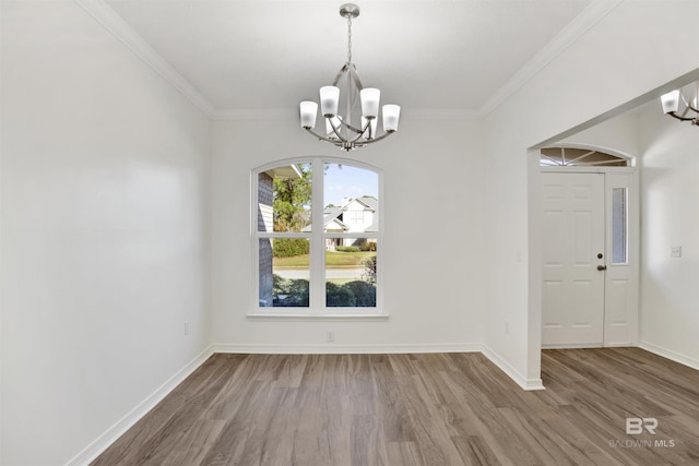 unfurnished dining area featuring wood-type flooring, ornamental molding, and a notable chandelier