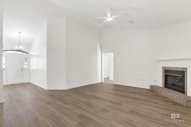 unfurnished living room featuring a fireplace, wood-type flooring, ceiling fan with notable chandelier, and lofted ceiling