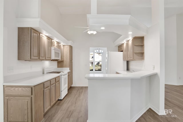 kitchen featuring white appliances, ceiling fan with notable chandelier, vaulted ceiling, light hardwood / wood-style floors, and kitchen peninsula