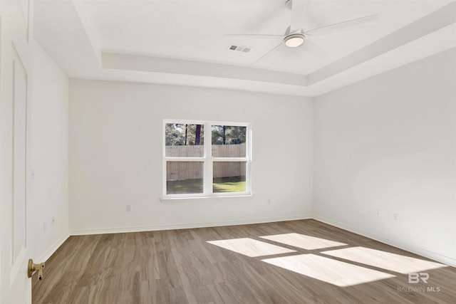 unfurnished room with hardwood / wood-style flooring, ceiling fan, and a tray ceiling