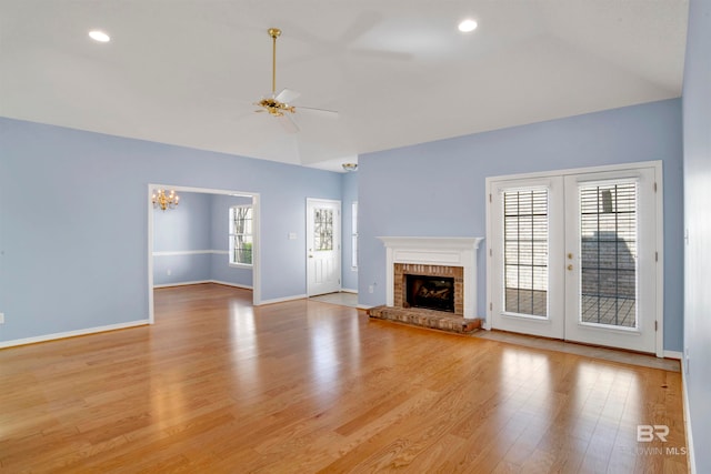 unfurnished living room featuring french doors, vaulted ceiling, a brick fireplace, light hardwood / wood-style floors, and ceiling fan