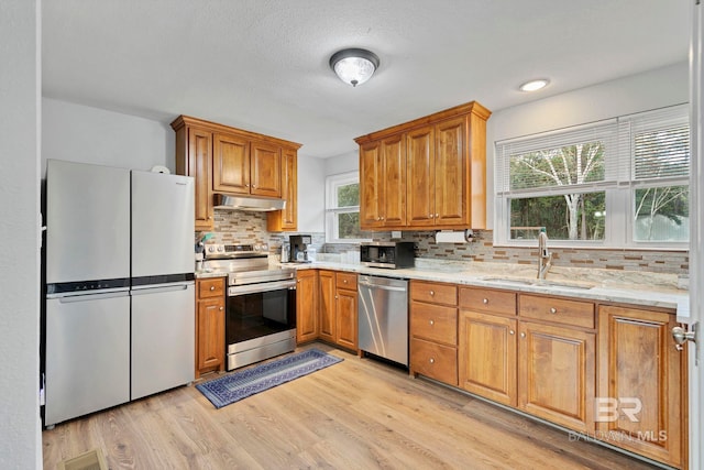 kitchen featuring sink, light hardwood / wood-style flooring, stainless steel appliances, light stone counters, and decorative backsplash