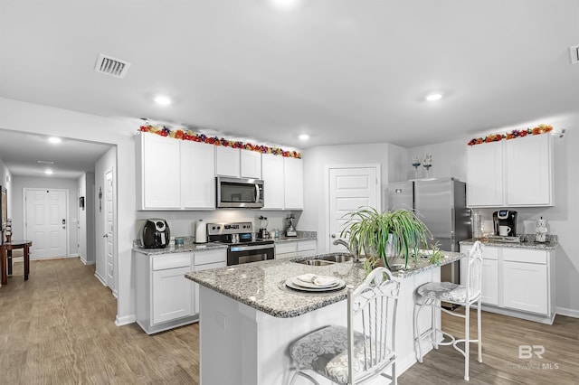 kitchen with stainless steel appliances, light hardwood / wood-style floors, sink, a center island with sink, and a breakfast bar area