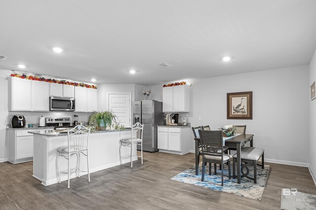 interior space with white cabinetry, hardwood / wood-style flooring, stainless steel appliances, and an island with sink