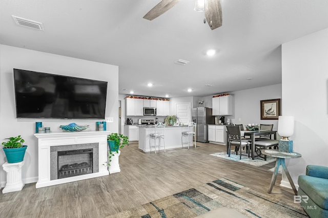 living room with light hardwood / wood-style floors, ceiling fan, and a fireplace