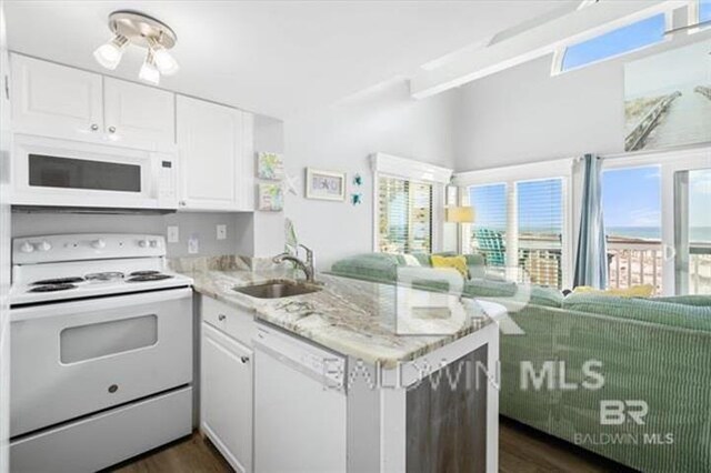 kitchen featuring white appliances, white cabinets, open floor plan, a peninsula, and a sink