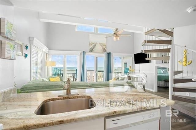 kitchen featuring a ceiling fan, light stone counters, open floor plan, white dishwasher, and a sink