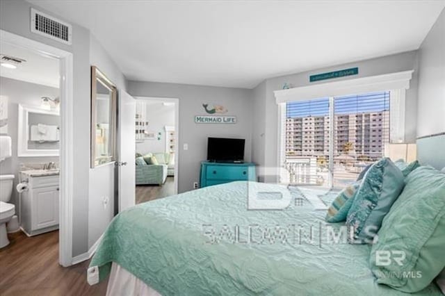 bedroom with ensuite bath, wood finished floors, visible vents, and baseboards