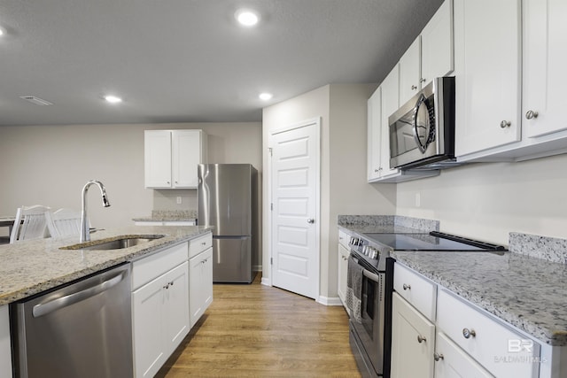 kitchen featuring stainless steel appliances, a sink, light wood-style flooring, and white cabinets