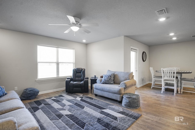 living room featuring ceiling fan, a textured ceiling, wood finished floors, and visible vents