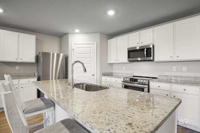 kitchen featuring a center island with sink, stainless steel appliances, recessed lighting, a sink, and light stone countertops