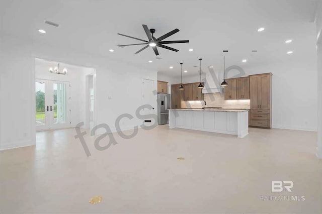 kitchen featuring pendant lighting, high end refrigerator, ceiling fan with notable chandelier, tasteful backsplash, and a kitchen island