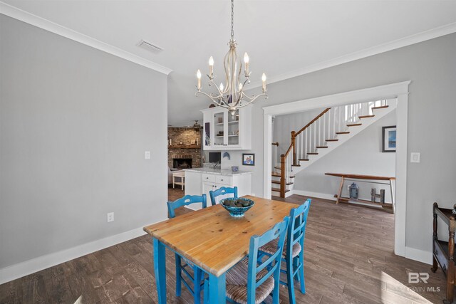 dining area featuring stairway, wood finished floors, visible vents, crown molding, and a large fireplace