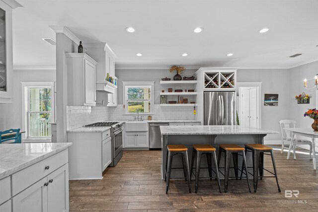 kitchen featuring crown molding, decorative backsplash, a kitchen breakfast bar, stainless steel appliances, and open shelves