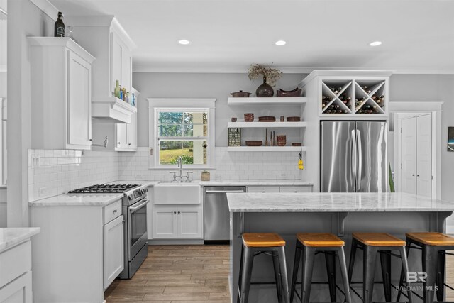 kitchen featuring a kitchen bar, decorative backsplash, appliances with stainless steel finishes, white cabinetry, and a sink