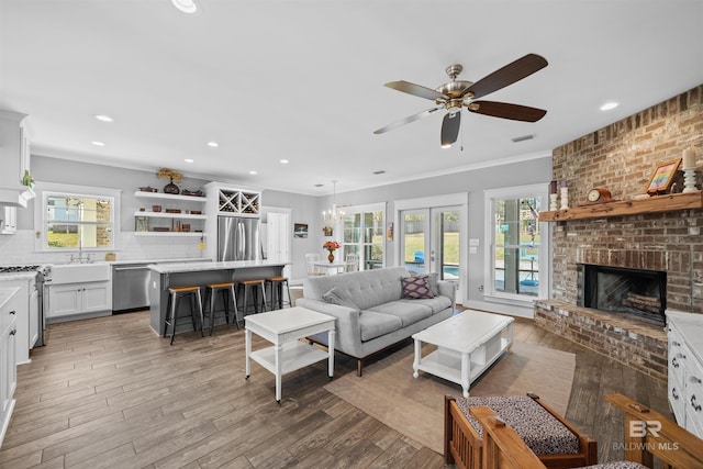 living area with visible vents, light wood-style flooring, french doors, crown molding, and a brick fireplace