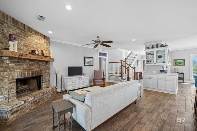 living room featuring a fireplace, dark wood-style floors, stairs, and ornamental molding