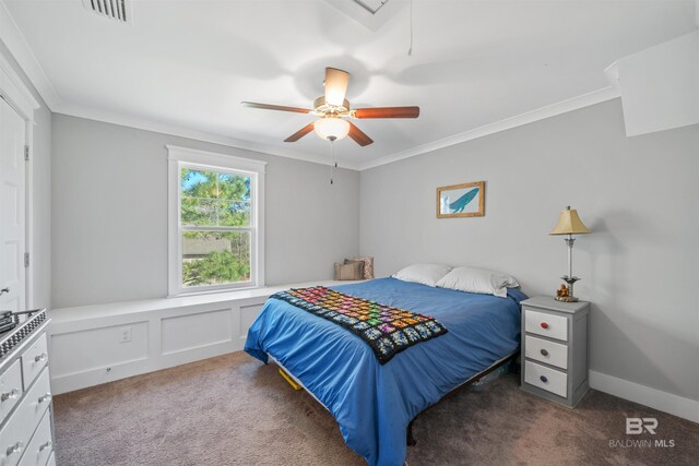 carpeted bedroom with visible vents, crown molding, a decorative wall, attic access, and ceiling fan