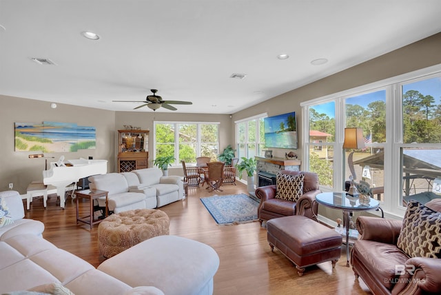 living room with ceiling fan, visible vents, a glass covered fireplace, and light wood finished floors
