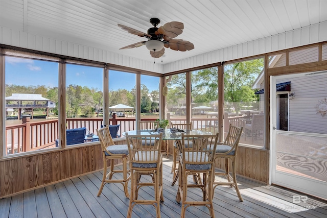 sunroom featuring a water view, outdoor dining space, and ceiling fan