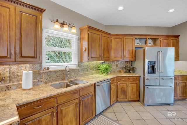 kitchen featuring light tile patterned floors, appliances with stainless steel finishes, brown cabinetry, and a sink