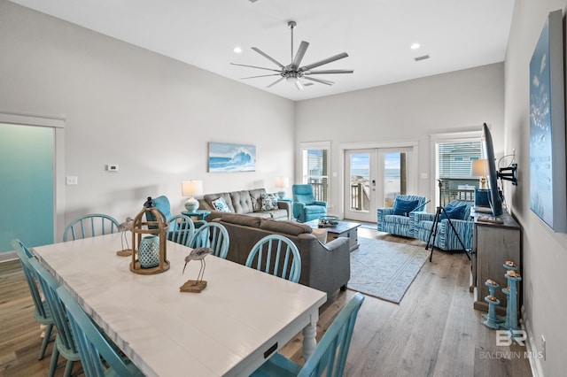 dining area featuring french doors, ceiling fan, light hardwood / wood-style flooring, and a towering ceiling