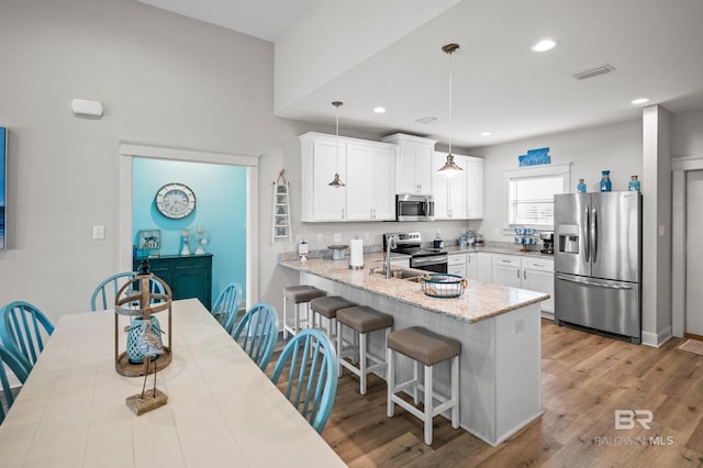 kitchen with a breakfast bar, decorative light fixtures, kitchen peninsula, stainless steel appliances, and white cabinets