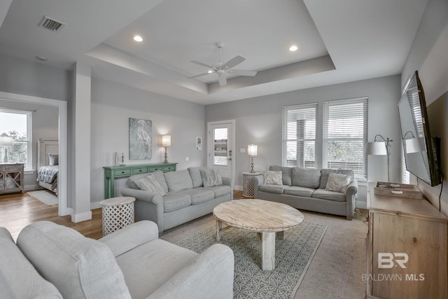 living room featuring light hardwood / wood-style flooring, a raised ceiling, and ceiling fan