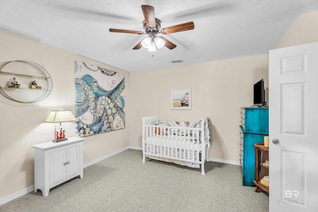 bedroom featuring a textured ceiling, ceiling fan, light colored carpet, and a crib