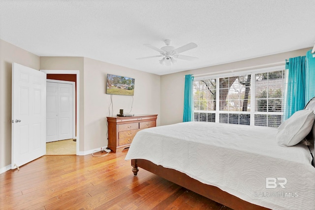 bedroom featuring a textured ceiling, light wood finished floors, a ceiling fan, and baseboards