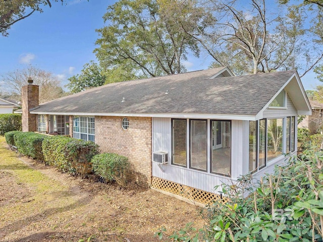 rear view of house featuring a sunroom, brick siding, a chimney, and roof with shingles