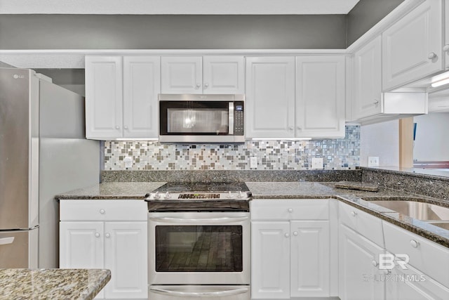 kitchen featuring white cabinets, dark stone counters, appliances with stainless steel finishes, backsplash, and a sink