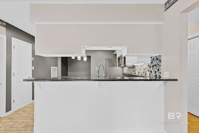 kitchen with visible vents, dark stone counters, decorative backsplash, stainless steel microwave, and a peninsula