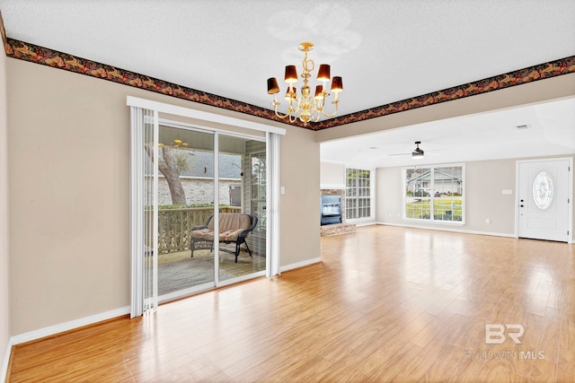 unfurnished living room featuring an inviting chandelier, a glass covered fireplace, a textured ceiling, light wood-type flooring, and baseboards