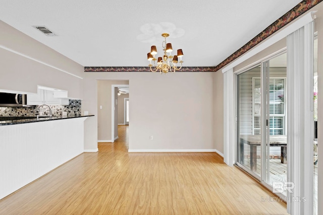 spare room featuring light wood finished floors, visible vents, a sink, baseboards, and ceiling fan with notable chandelier