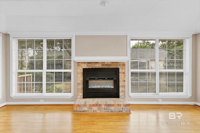 unfurnished living room with a wealth of natural light, a fireplace, baseboards, and wood finished floors