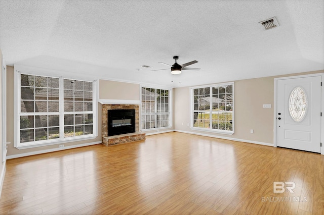 unfurnished living room with visible vents, a ceiling fan, a glass covered fireplace, a textured ceiling, and wood finished floors