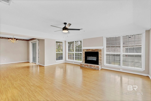 unfurnished living room with ceiling fan with notable chandelier, a brick fireplace, visible vents, and wood finished floors