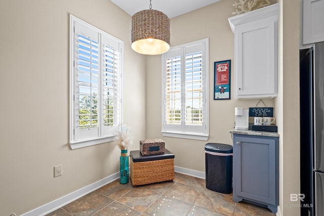 kitchen featuring white cabinetry, stainless steel fridge, decorative light fixtures, and a wealth of natural light