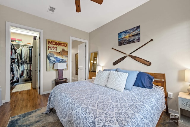 bedroom featuring a walk in closet, a closet, ceiling fan, and dark hardwood / wood-style flooring