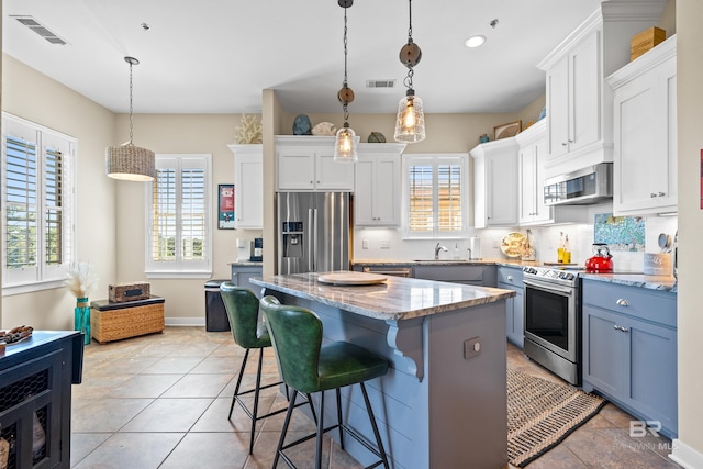 kitchen featuring white cabinets, a breakfast bar area, a kitchen island, stainless steel appliances, and decorative light fixtures