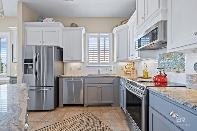 kitchen with decorative backsplash, stainless steel appliances, sink, light stone countertops, and white cabinetry