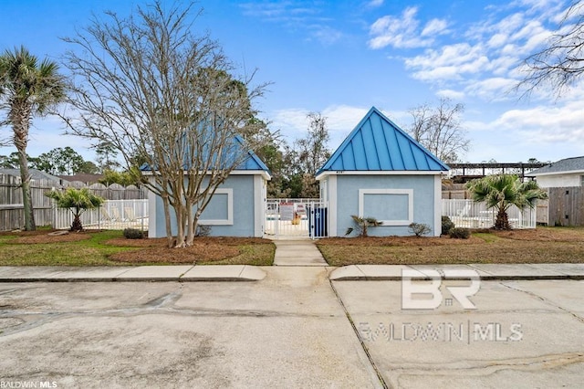 view of front of property with a standing seam roof, a fenced front yard, metal roof, and stucco siding