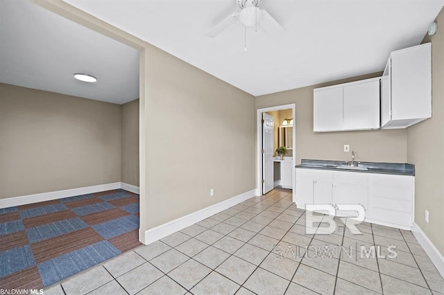 kitchen with light tile patterned floors, baseboards, white cabinets, ceiling fan, and a sink