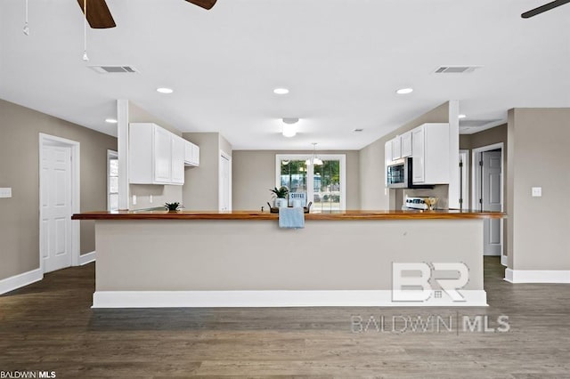 kitchen with butcher block countertops, dark wood-style flooring, white cabinetry, baseboards, and stainless steel microwave